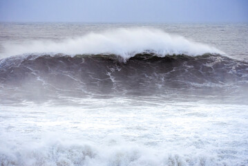 Big waves crashing on the sea with greenish blue color during a cloudy day
