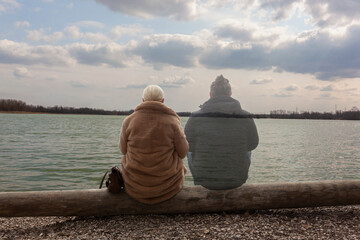 Lonely woman sitting by the lake with ghost of a man sitting by her side, staring in the distance - obrazy, fototapety, plakaty