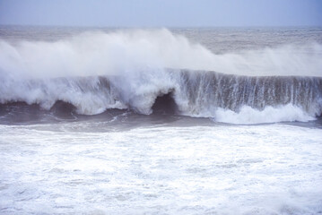 Big waves crashing on the sea with greenish blue color during a cloudy day