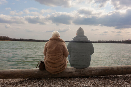 Lonely woman sitting by the lake with ghost of a man sitting by her side, staring in the distance
