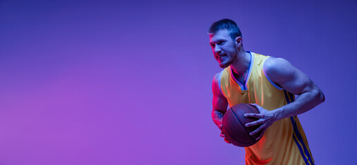 Fototapeta premium Studio shot of muscled man, basketball player training with ball isolated on purple background in neon light. Goals, sport, motion, activity concepts.
