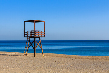 Wooden brown coastguard watchtower on the beach with blue sea in the background
