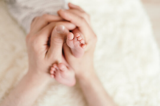 small legs of a newborn baby in the hands of his father. close-u