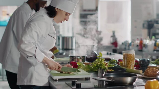 Authentic chef preparing garlic clove to add on delicious food, cooking meal in frying pan. Female cook using raw ingredients to make aromatic gourmet dish, culinary recipe. Handheld shot.