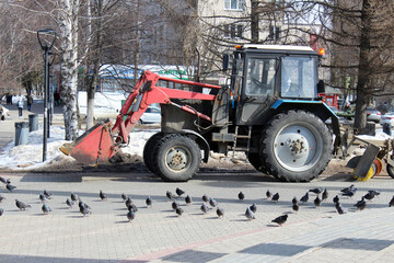 Obraz na płótnie Canvas the tractor rides on spring square and cleans the streets nearby pigeons walk on the roads