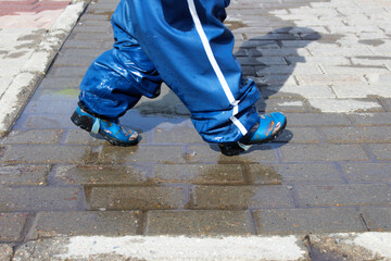 a little boy in blue rubber boots runs through puddles