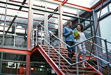 Communication is the key to success. Two colleagues walking side by side down stairs in their building.