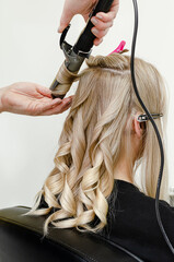 Fototapeta premium Stylist making a hairdo with hair curler for blond woman after hair dyeing. Beauty salon concept.