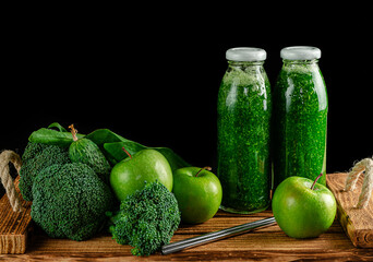 Bottles of green smoothie with ingredients on black background. Alkaline diet concept. Copy space