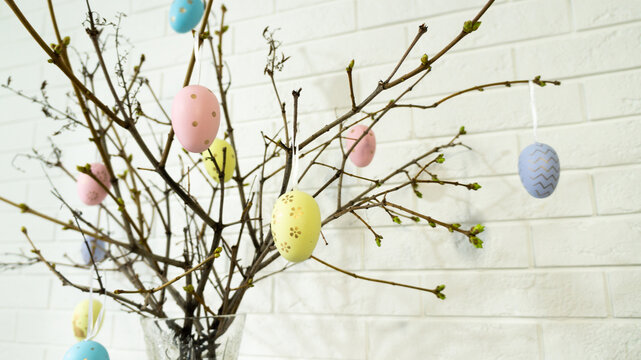 Creative composition with Easter eggs hanging on tree branches near a white brick wall. High quality photo