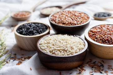 Different types of rice grains put in a wooden cup placed on a white cloth, concept of food and health.