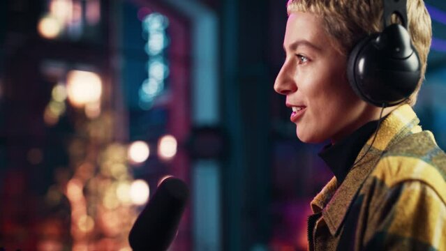 Confident Young Female Talking Into Microphone While Recording Radio Show from Her Loft Apartment. Happy Woman with Short Hair Talking on Camera and Recording Podcast Live on Social Media.