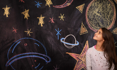 Let your imagination take you anywhere. Shot of a little girl standing in front of a chalkboard drawing.