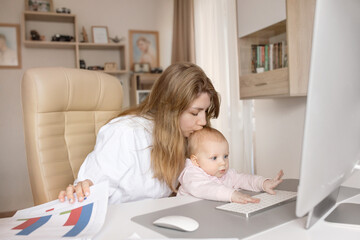 Fototapeta na wymiar Working young mother in maternity leave work remotely or study at home on computer while infant daughter hold papers and looking at screen. Modern day mother of little child sit at desk use gadgets