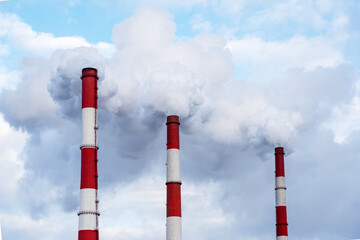 Three chimneys with a lot of toxic smoke against a blue sky during the day. Environment protection.