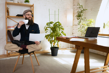 Young bearded man, office clerk having fun, doing yoga on wooden table in modern office at work time with gadgets. Concept of business, healthy lifestyle, sport, hobby - obrazy, fototapety, plakaty