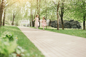 two little sisters are running along the path of the city park.