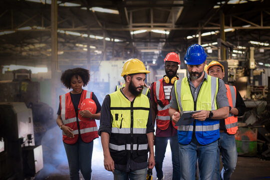 group of diversity teamwork, engineers, technician and workers team in safety uniform having discussion while walking through heavy industry manufacturing factory.	