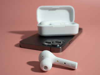 White wireless headphones and phone on a pink background.