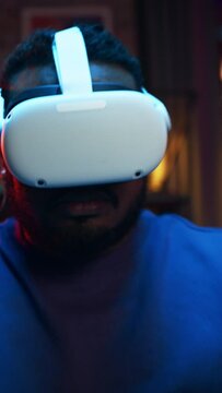 Vertical Portrait: Young Stylish Black Man Putting On Virtual Reality Headset. African American Man Sitting on a Sofa at Home in the Evening, Playing VR Video Games. Dramatic Zoom In Shot.
