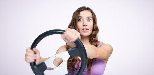 A young beautiful girl turns a car steering wheel making a maneuver. On light pink background....