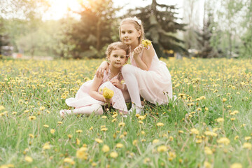 two little sisters with bouquets of dandelions sitting in a meadow.