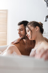 Brunette woman hugging boyfriend in bath with foam at home.