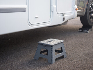 A portable collapsible step has been placed on ground outside a motorhome recreational vehicle to aid entry to the habitation door.