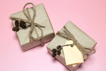 Two kraft paper gift boxes and an empty tag for text on a table on a pink background.