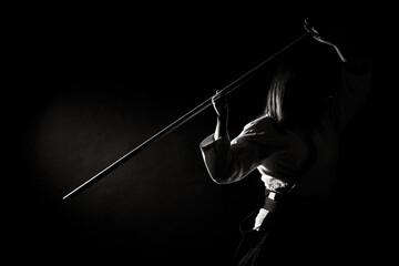 A girl in black hakama standing in fighting pose with wooden sword bokken over dark background....
