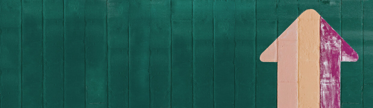 Hand Painted Stiped Magenta Yellow Skin Colored Up Arrow Over A Wide Blue Green Painted Stone Wall