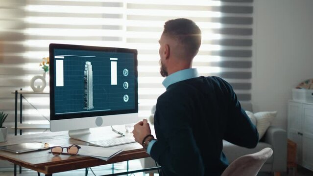 Young architect designer is working on building a 3d model plan using a professional software, stretching his arms and back after a long work