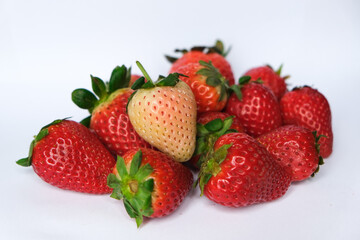 Ripe white/pink strawberry on a pile of red strawberries isolated on white background