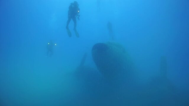 Image of divers floating among plane wrecks under the sea.