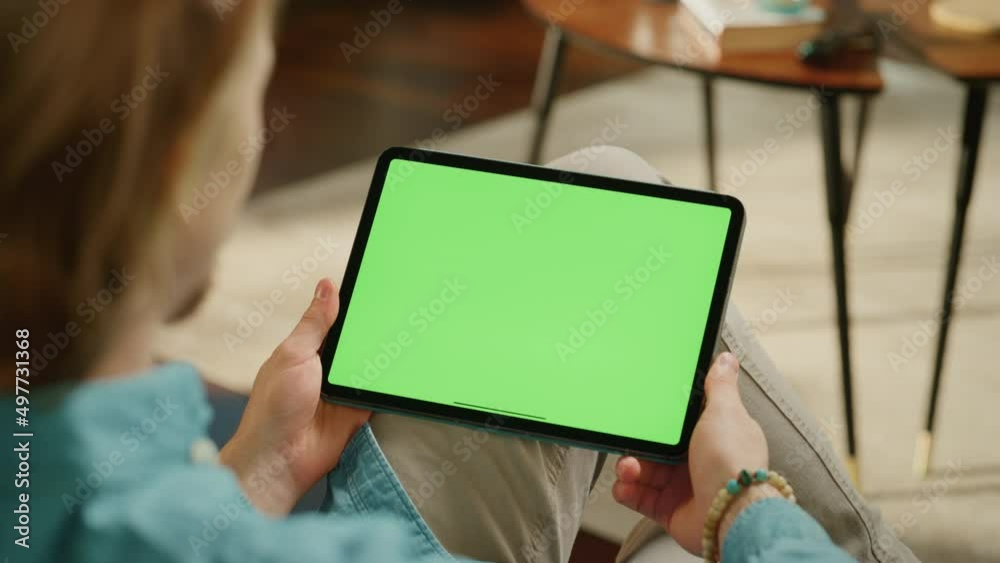 Aufkleber young man holding tablet computer with green screen mock up display. male relaxing at home, watching