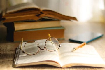Open book, mechanical pencil, reading glasses, mobile phone and strack of books on the desk....