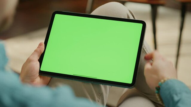 Young Man Scrolling and Tapping on Content on Tablet Computer with Green Screen Mock Up Display. Male Relaxing at Home, Reading Social Media Posts on Mobile Device. Close Up Over the Shoulder Footage.