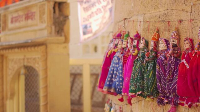Closeup shot of colorful human shaped Puppets wearing colorful traditional clothes hanging against the wall in Jaisalmer, Rajasthan, India. View of traditional homemade dolls in streets of Rajasthan.