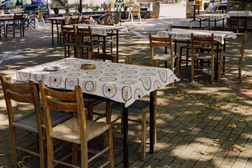 Empty tavern outdoors seating area with wooden chairs and tables on a village square in Greece.