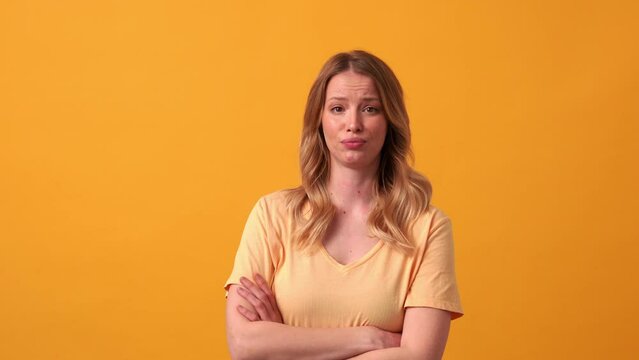 Angry blonde woman wearing yellow t-shirt saying what at the camera in the orange studio