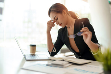 Very stressed business asian woman sitting in front of her computer looking at a large pile of...