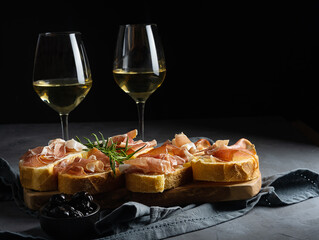 Italian appetiser - bruschetta with prosciutto, white wine, rosemary branch and black olives