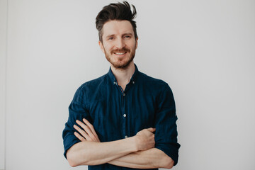 Handsome young man in a dark blue shirt by a light wall. Place for text.