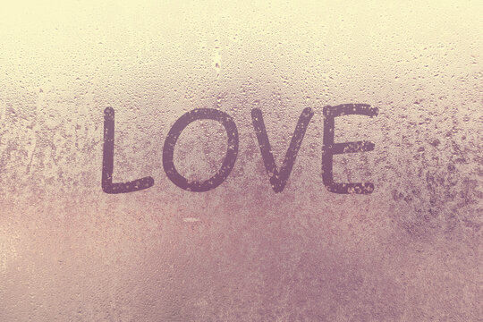 Word Love and shape of heart are drawn with a finger on fogged window glass. Valentine's Day, Valentine card creative. Blur Love sign drawing, blurred background. February its month love, concept.