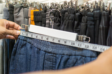 Woman's hand is measuring the waist of the pants with a tape measure in clothing store.