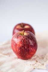 Two juicy and fresh red apples of biological origin arranged one behind the other on the white table. Vertical photo.