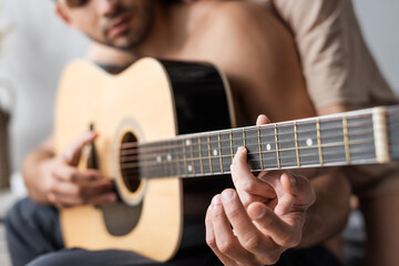 Fototapeta premium Cropped view of blurred couple playing acoustic guitar at home.