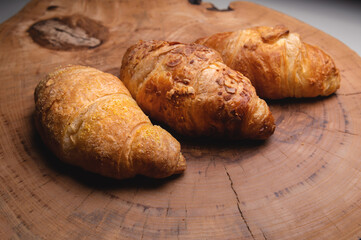 Close-up of a pile of three croissants on a wooden board against a dark background. Delicious and healthy breakfast