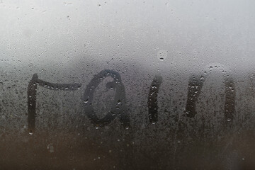 A word Rainy is written on the sweaty foggy window. Water droplets condensation background of dew...