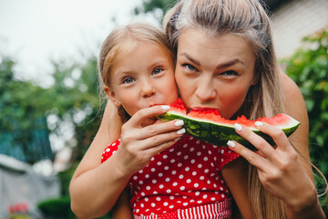 happy mother and daughter eating watermelon in garden.